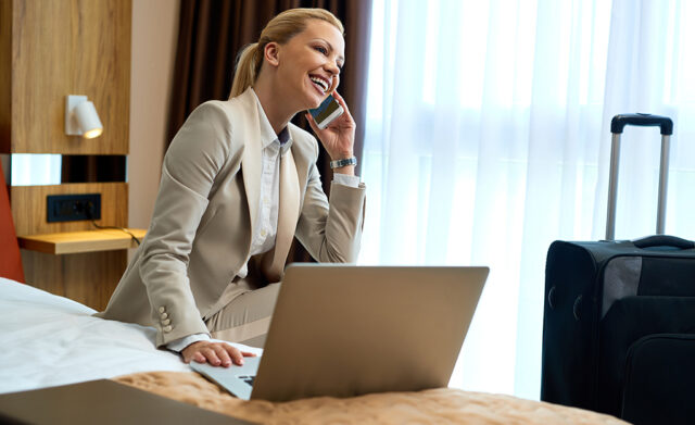 Happy businesswoman talking on the phone while using laptop in h